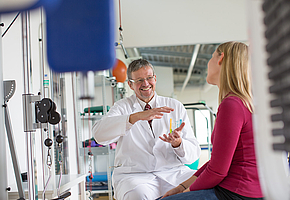 Der Chefarzt der Rehaklinik Heidelberg-Königstuhl sitzt bei einer Patientin im Fitnessraum und spricht mit ihr.